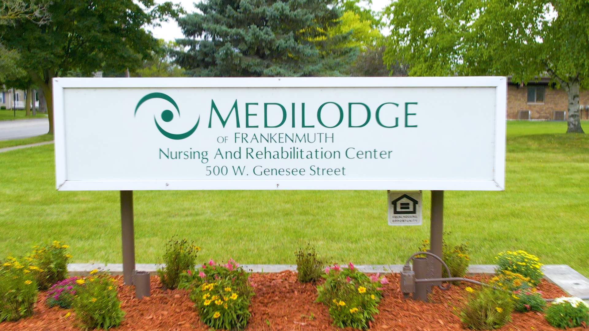 Medilodge of Frankenmuth sign board with plants and trees on the background.