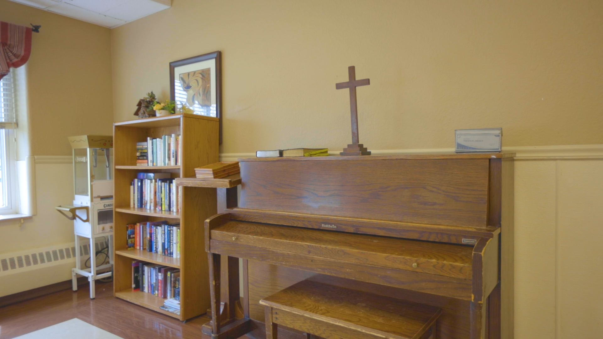 Piano with cross on top and book shelf on the side.